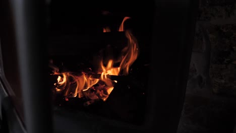 hand reaches in to place stick on orange red hot wood burning on small cabin household fire, slow motion footage as sparks and embers fly out with door slightly open.