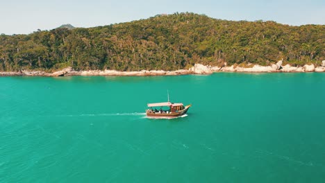 Vista-Aérea-Lateral-De-Un-Barco-Turístico-Que-Pasa-Por-El-Color-Turquesa-Del-Agua-Y-El-Paradisíaco-Paisaje-De-La-Selva-Tropical-Del-Mar