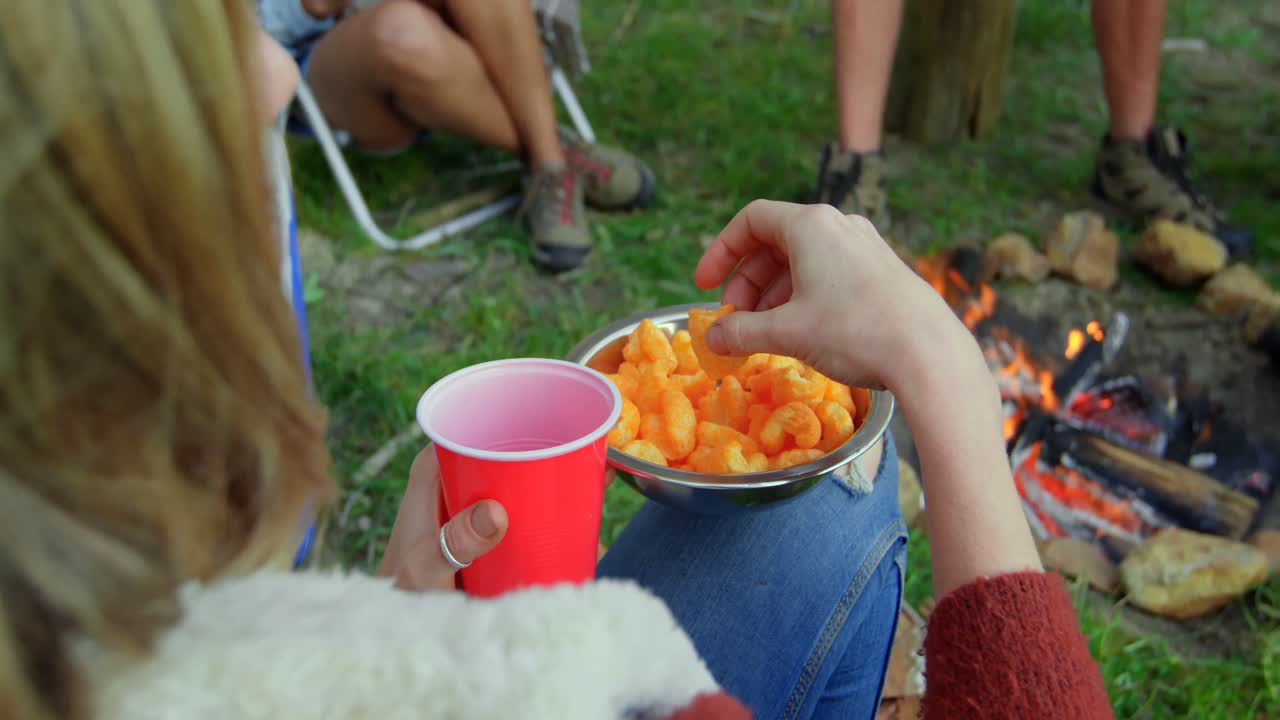 mujer comiendo comida mientras estaba sentada cerca de una hoguera en el bosque 4k