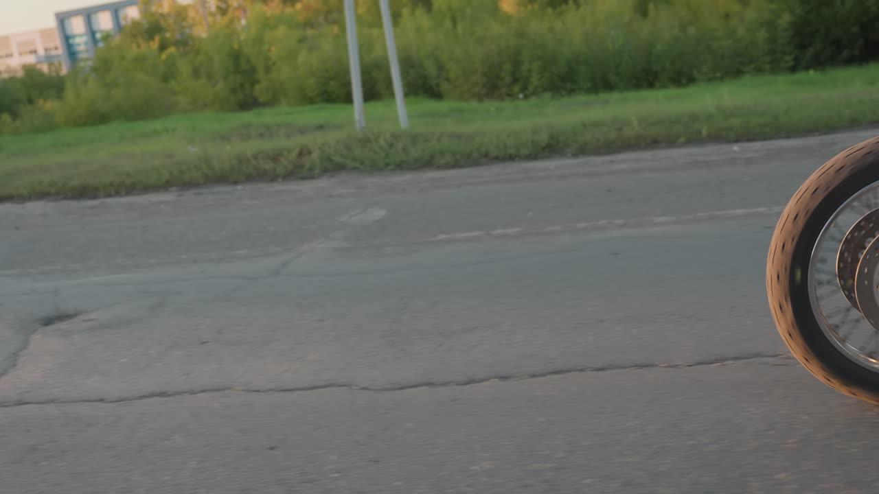 Motorcycle rider with passenger in helmets and leather jackets traveling on roadside during sunset, chrome details of bike shining while moving past road signs and symbolizing lifestyle