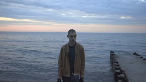 front view of a young man walking slowly towards the camera with beautiful sea and sunset in the background - medium shot