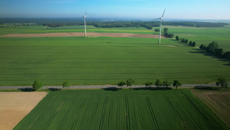 Windmills-over-fields,-aerial-drone-pull-out