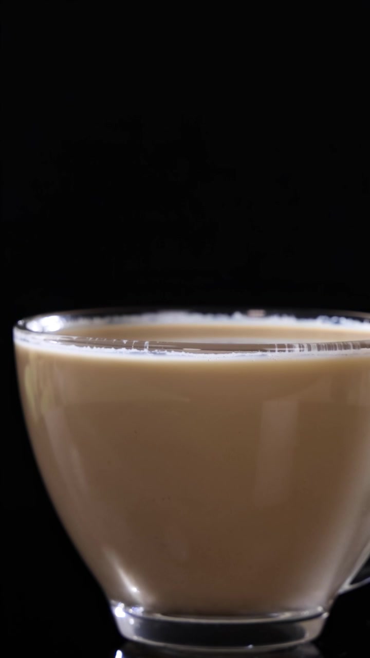 Una tazza di vetro piena di caffè latte poggia su uno sfondo nero, evidenziandone la consistenza cremosa e il design elegante