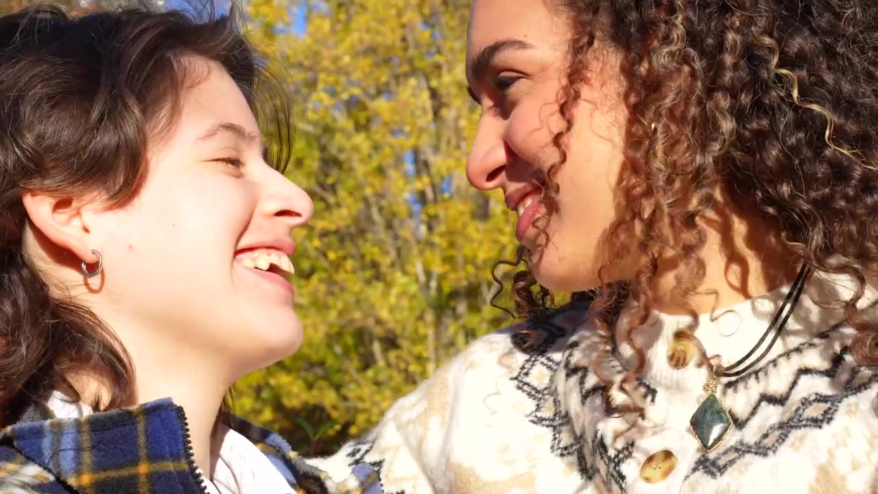 Happy multicultural lesbian couple smiling and talking outdoors during a sunny autumn day