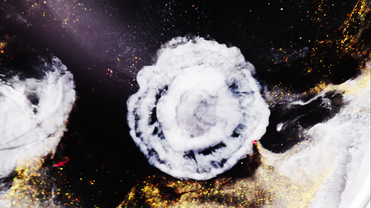Polvere dorata e pittura nera che si mescolano creando uno sfondo astratto simile a una galassia