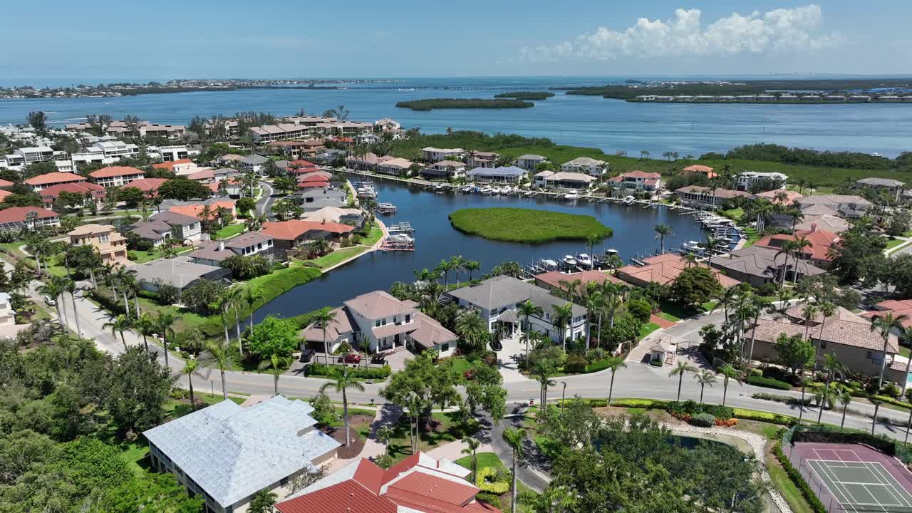 Luxurious coastal community with waterfront homes, tennis courts and lush greenery. Noble apartments, villas and private river with island. Cortez, Florida in summer. Aerial wide shot.