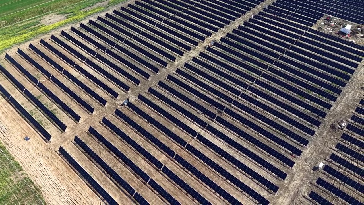Droneoptagelser viser rækker af solpaneler på tværs af en stor energipark under klar himmel, der fremviser ren teknologi, bæredygtig energiproduktion og geometriske mønstre i sollys.