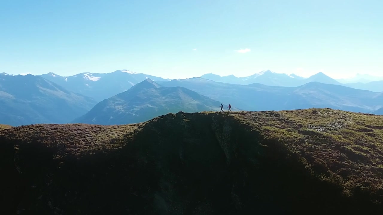 Ripresa ravvicinata con drone di due escursionisti con zaino che camminano lungo una cresta di montagna nelle Alpi. Avventura escursionistica estiva in uno splendido paesaggio montano