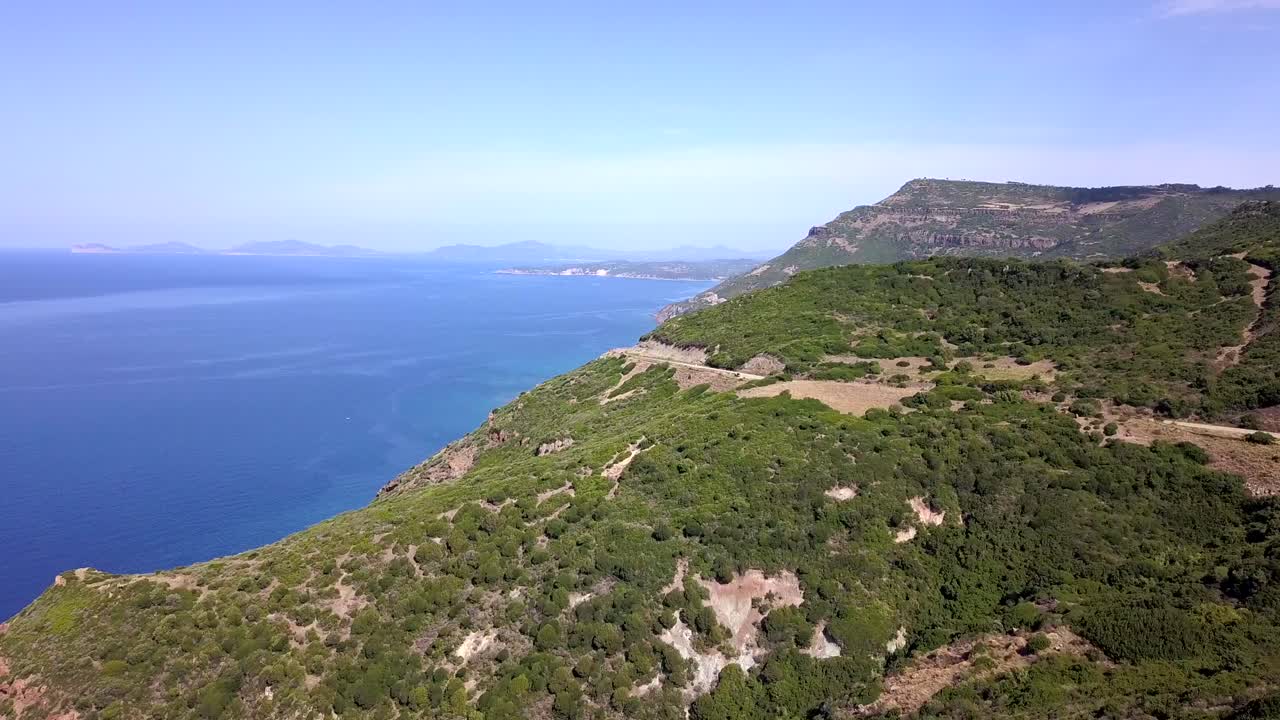 Drone Aerial shot, following the coastal road on a mediterranean landscape with stunning blue water and green hills, in Sardinia, Italy south of thes Spanish town of Alghero