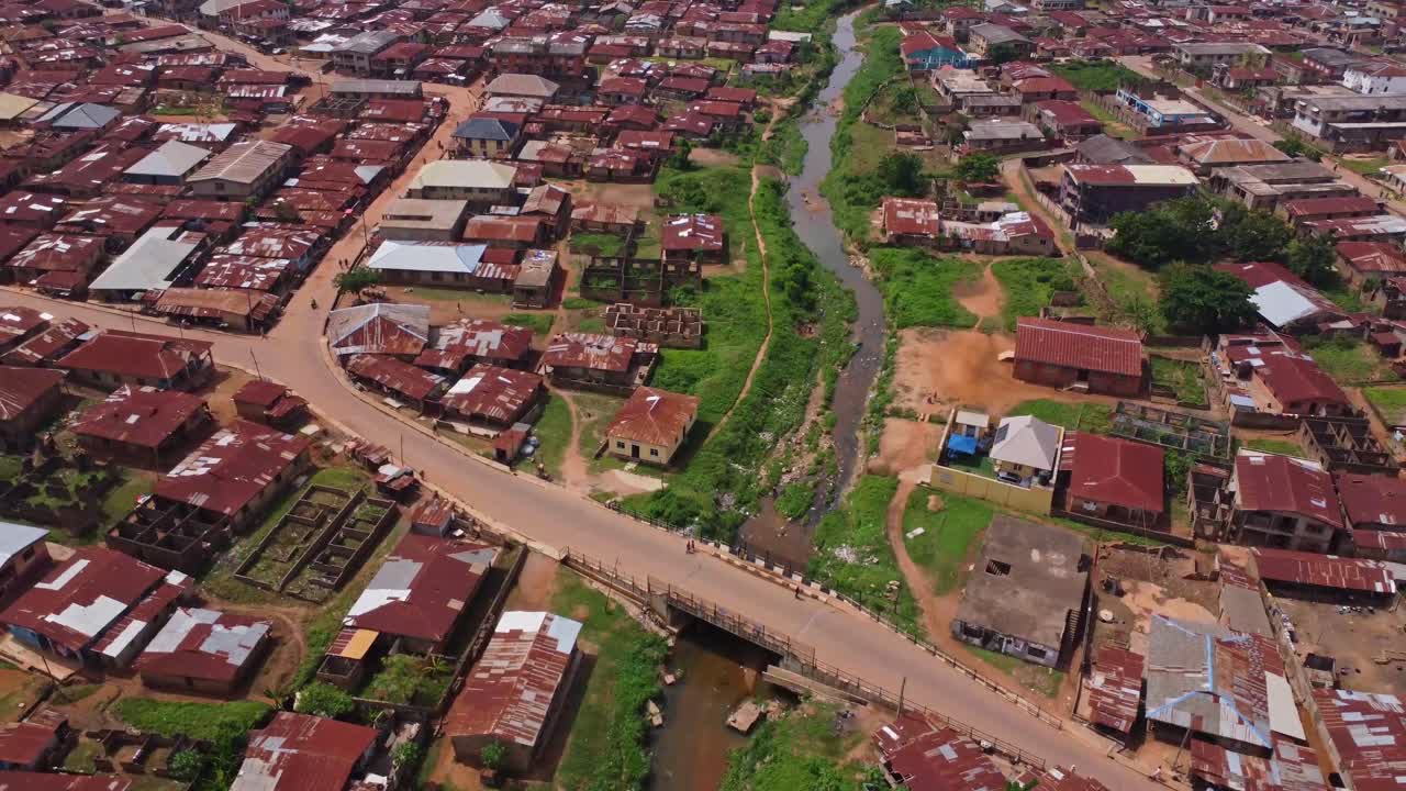 Jib up of motorcycles driving over a small bridge crossing a river in a small town in Ibadan, Nigeria on a sunny day
