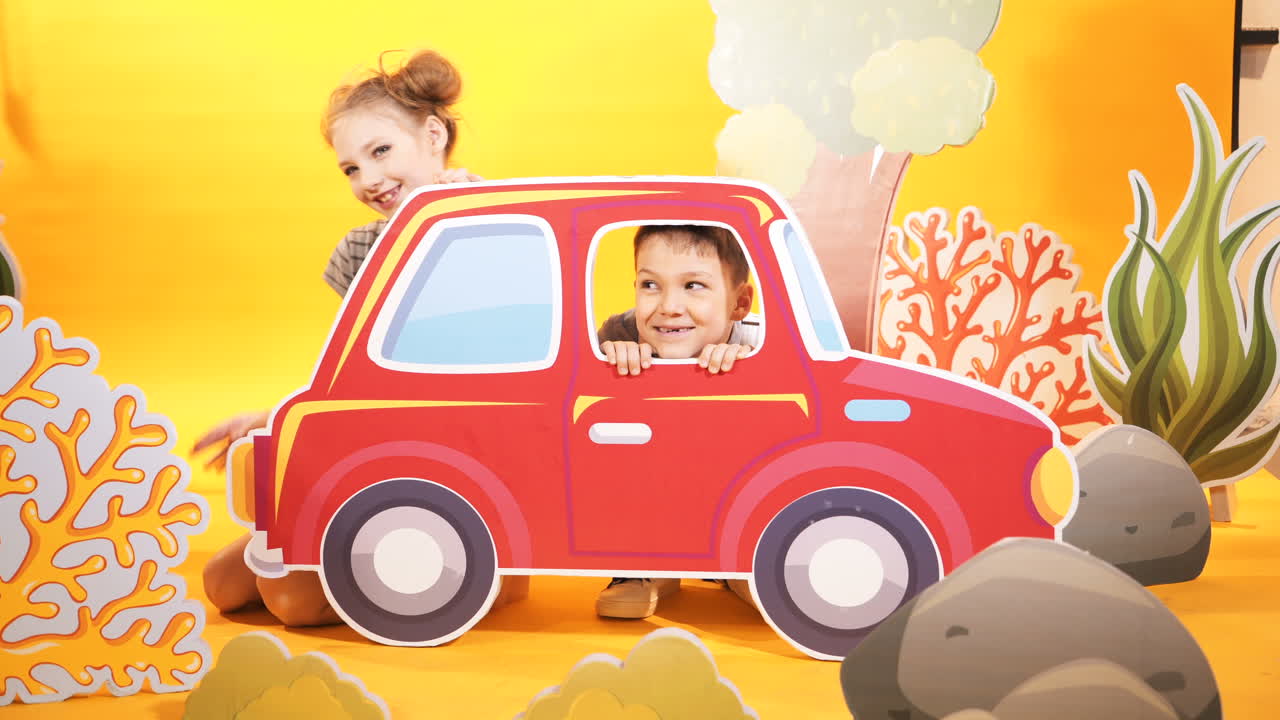 Bambini felici con una grande macchina giocattolo su uno sfondo di parete giallo brillante. Scenografia per bambini in studio
