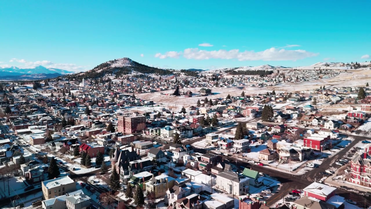 モンタナ州ビュートの都市のスプロール現象上空を飛行するドローンが、高地の山岳地帯に位置する歴史的な都市計画、鉱業遺産の建造物、広大な住宅街を捉える。