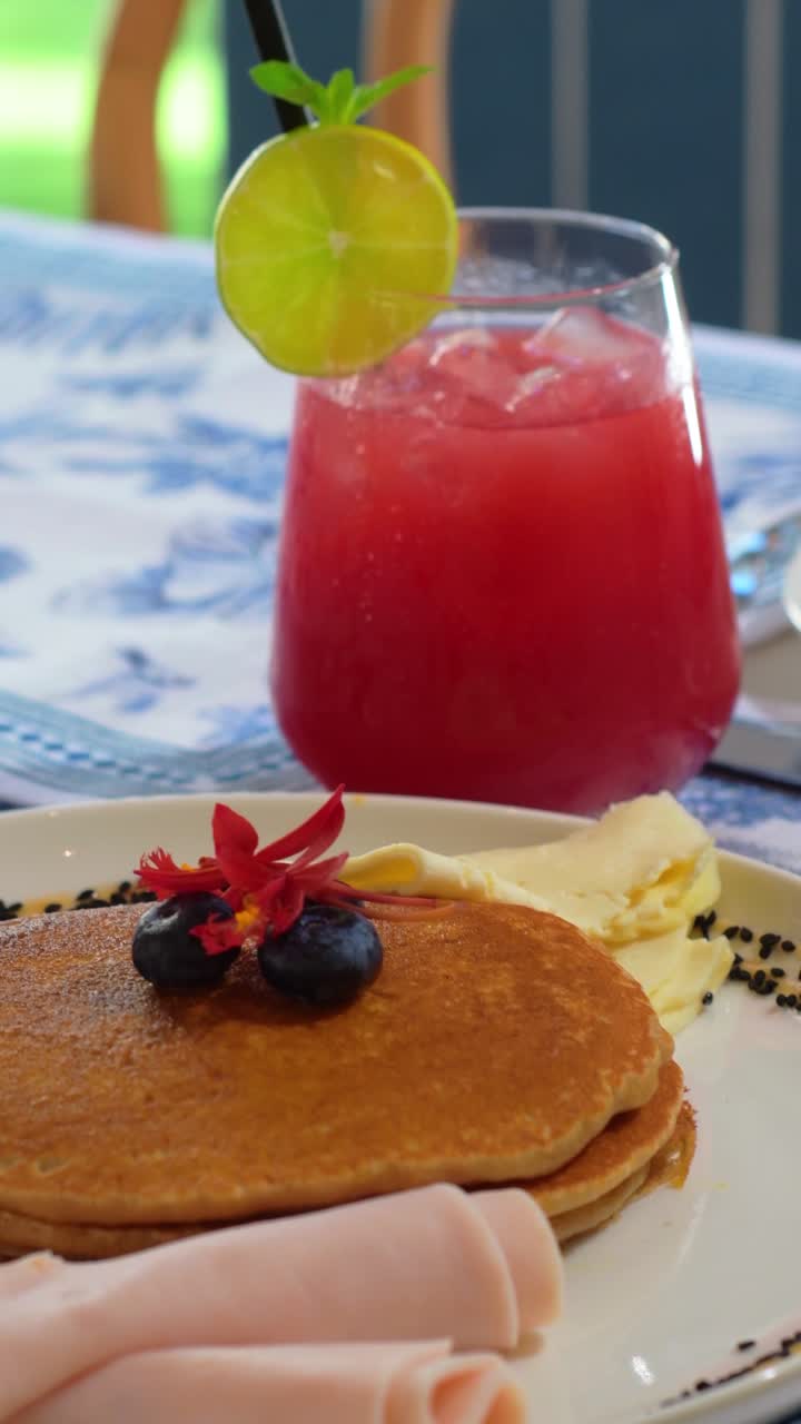 Tilt up of pancakes and strawberry juice on blue table set with modern styling