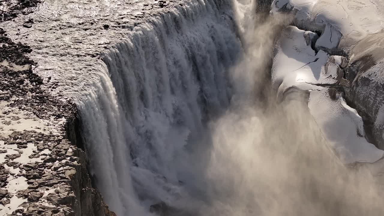 Powerful Dettifoss waterfall in Iceland, seen from an aerial perspective. Meltwater plunges into a rugged, snowy gorge.