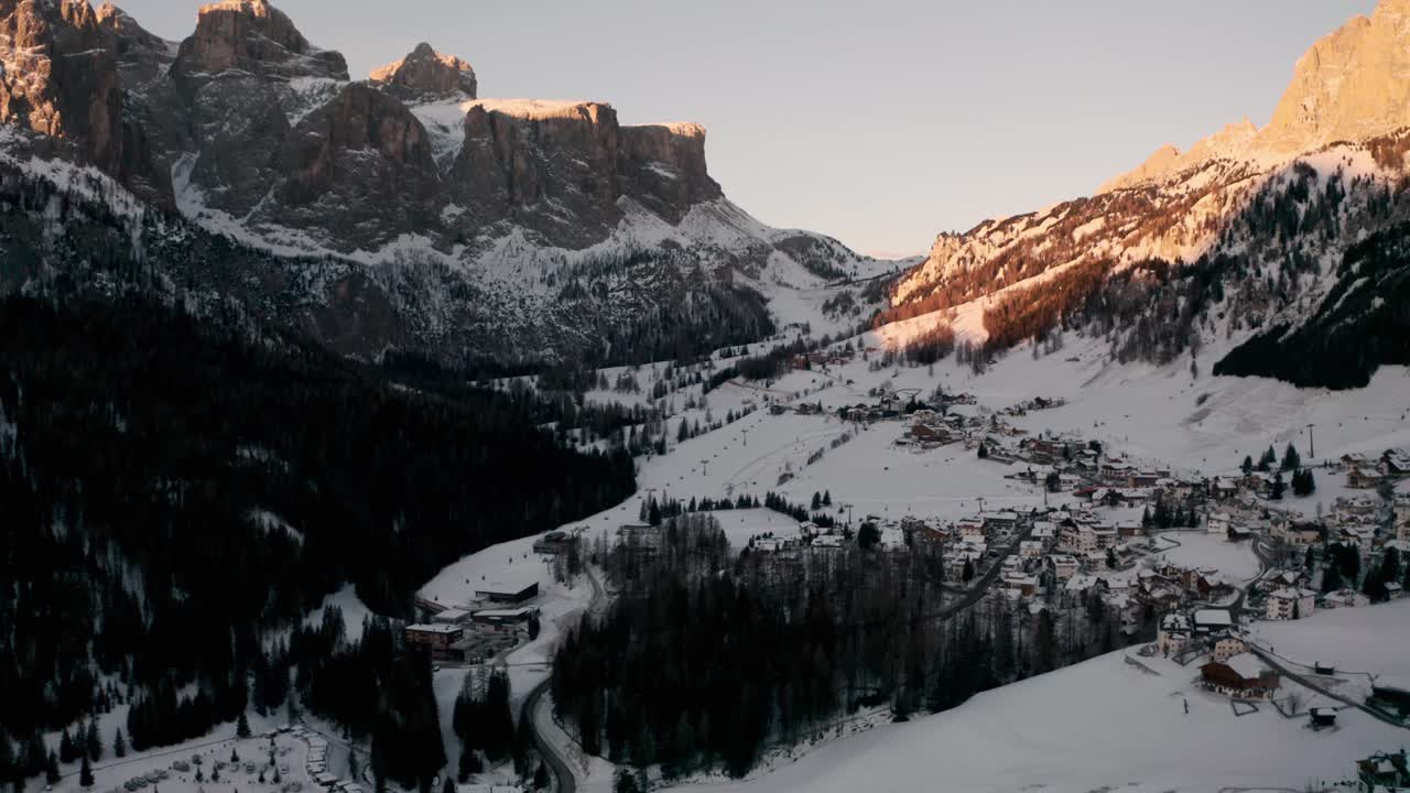 dolly back establece un disparo de drones sobre el pueblo de montaña de colfosco en invierno al amanecer.