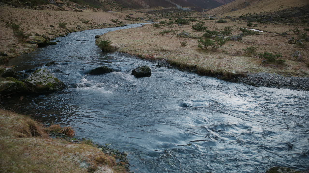 Um rio flui calmamente para um lago em um vale na Noruega em um dia de inverno ensolarado