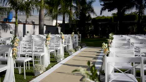 outdoor place decorated for a wedding ceremony, with white chairs placed over green grass, carpet in the center aisle decorated with flowers and veils, view from the altar