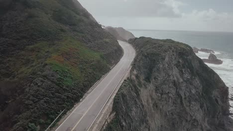 aerial drone view across south pacific highway following coastal route with views of the ocean waves alongside rocky terrain