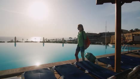 steadicam shot of woman with travel bag walking on recreation area along the pool