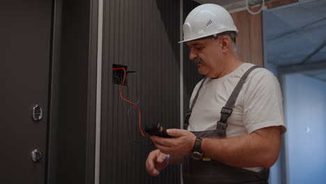 portrait electrician checks the operation of the wall control unit of lamps with the system of modern house after installation and repair