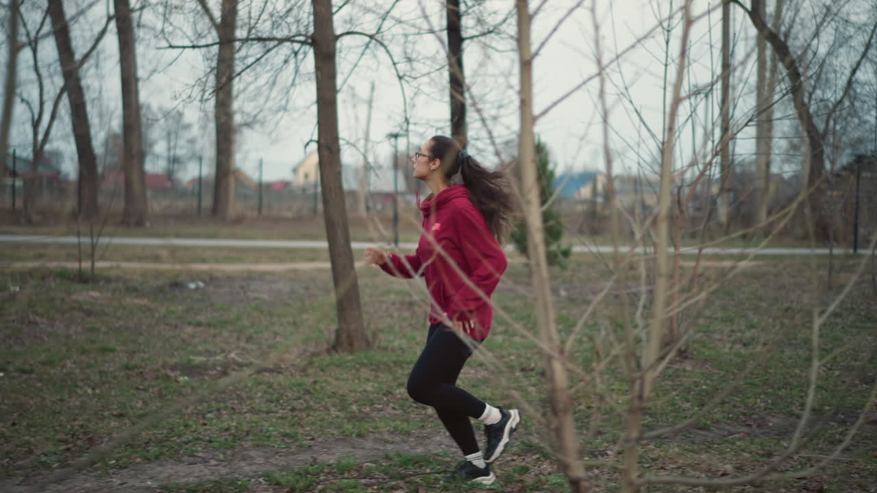 Female Runner Outdoors, Young Woman Exercising Along Park Pathway, Female Athlete In Red Hoodie Focusing On Run Pace, Young Woman With Glasses Jogging Through Fall Leaves During Training Session