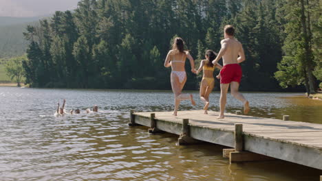 Amigos-Felices-Saltando-Del-Embarcadero-En-El-Lago-Chapoteando-En-El-Agua-Disfrutando-De-La-Libertad-Divirtiéndose-Aventura-De-Verano-En-Vacaciones