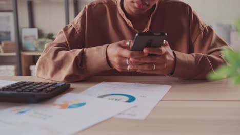 close up of businesswoman sitting while working on smart phone and calculating