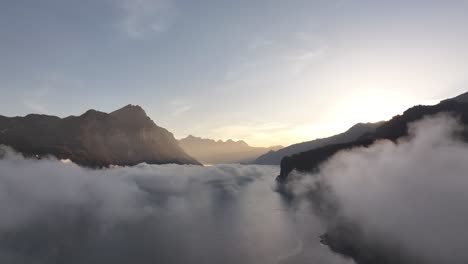 aerial image moving backward, revealing a phenomenal foggy sunrise over lake walensee, in the canton of st. gallen, switzerland.