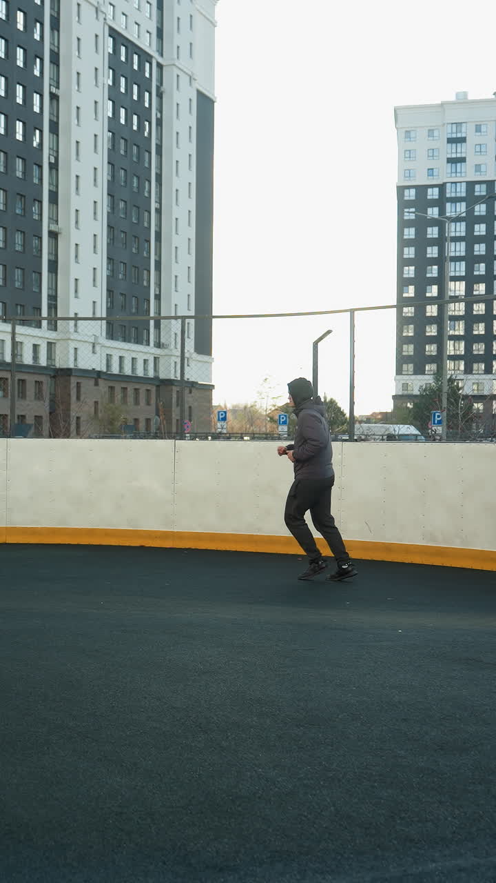 Wide view of a sportsman jogging in an outdoor arena featuring a soccer ball and goalpost with urban high-rise buildings in the background