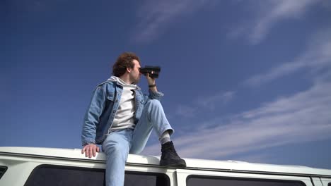 young boy looks around with a pair of binoculars on the roof of a caravan.