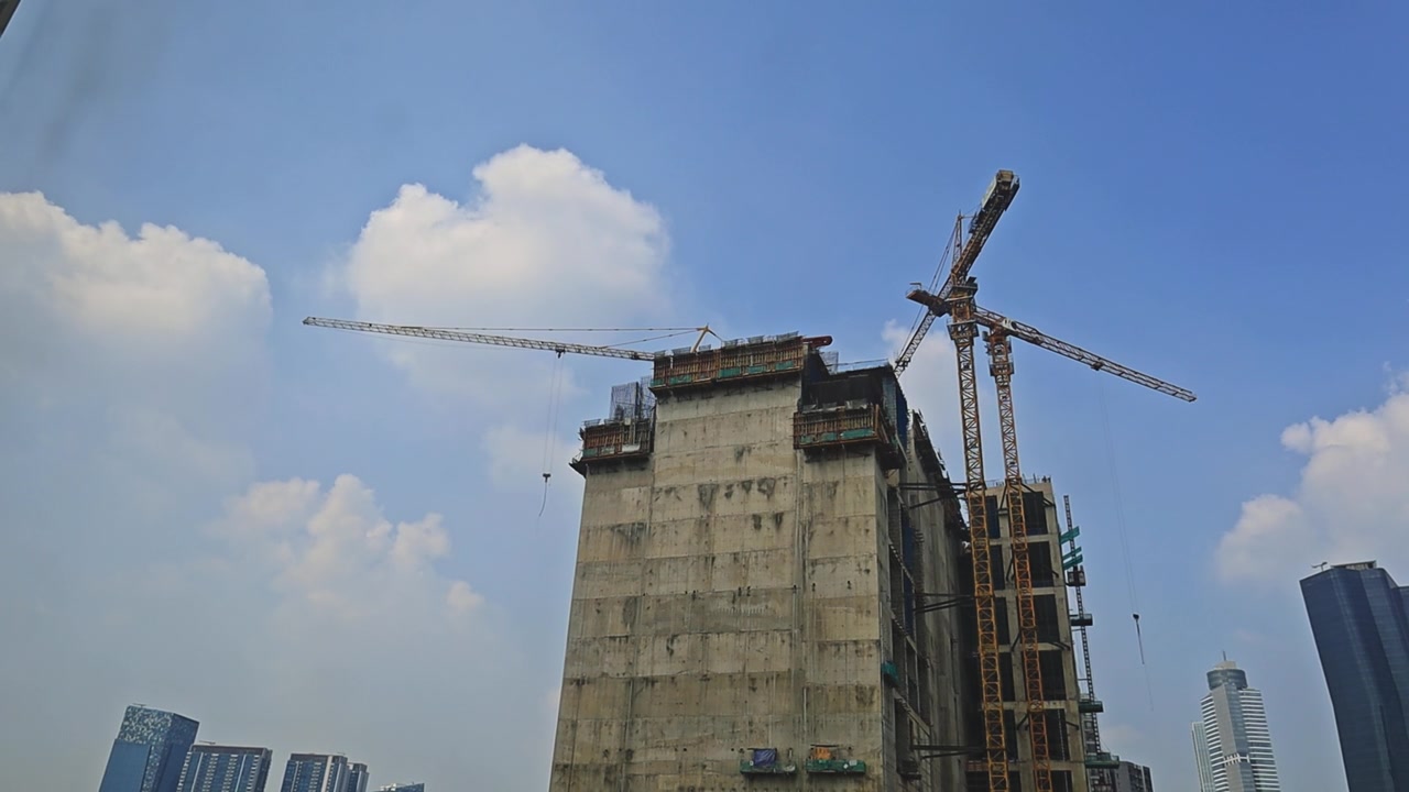 Grúas de construcción pesadas operando en la estructura de un edificio alto contra un cielo azul nublado