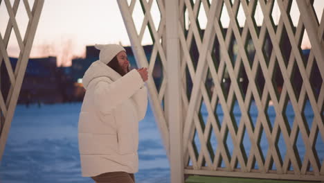 cheerful girl dancing in lit snowy pavilion at sunset wearing puffer coat beanie and headphones fluid moves in gentle breeze evoke joyful winter mood under twinkling lights and lattice glow