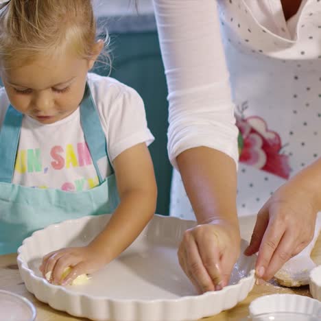 linda niña engrasando un plato para hornear