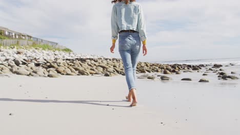 Vista-Trasera-De-Una-Mujer-De-Raza-Mixta-Caminando-Descalza-Por-La-Playa-Junto-Al-Mar.