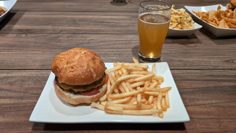 Delicious-fresh-burger-and-fries-with-beer-glass-on-wooden-table,-moving-forward-view