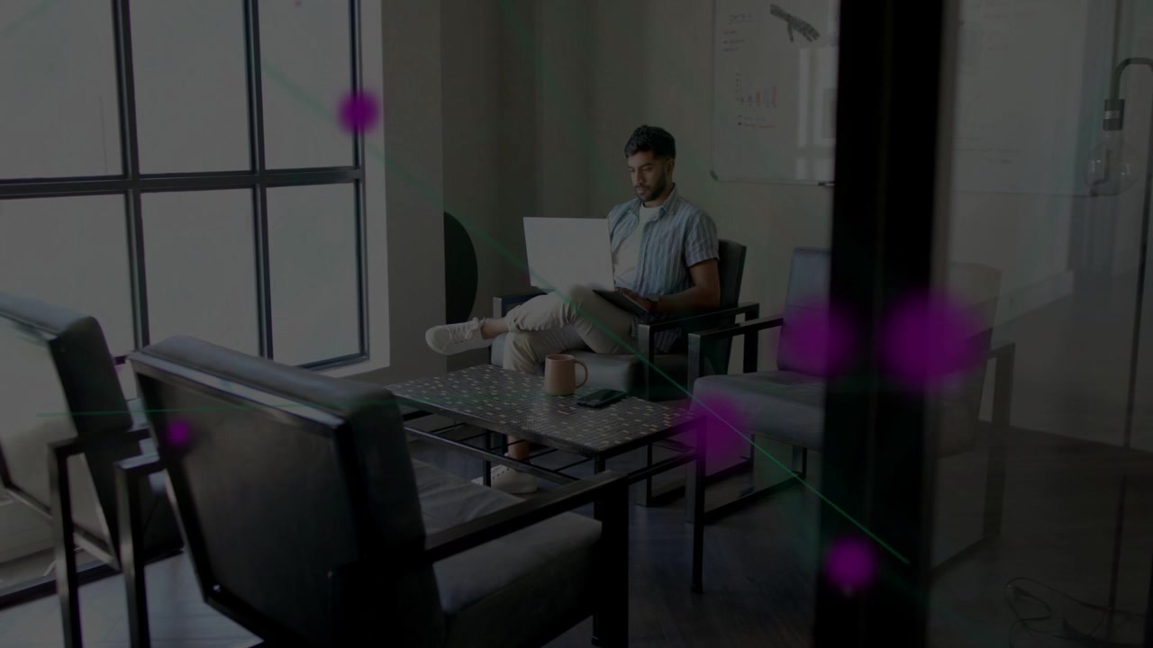 Office worker working on laptop in lounge, causing magenta circles growing across glass partition
