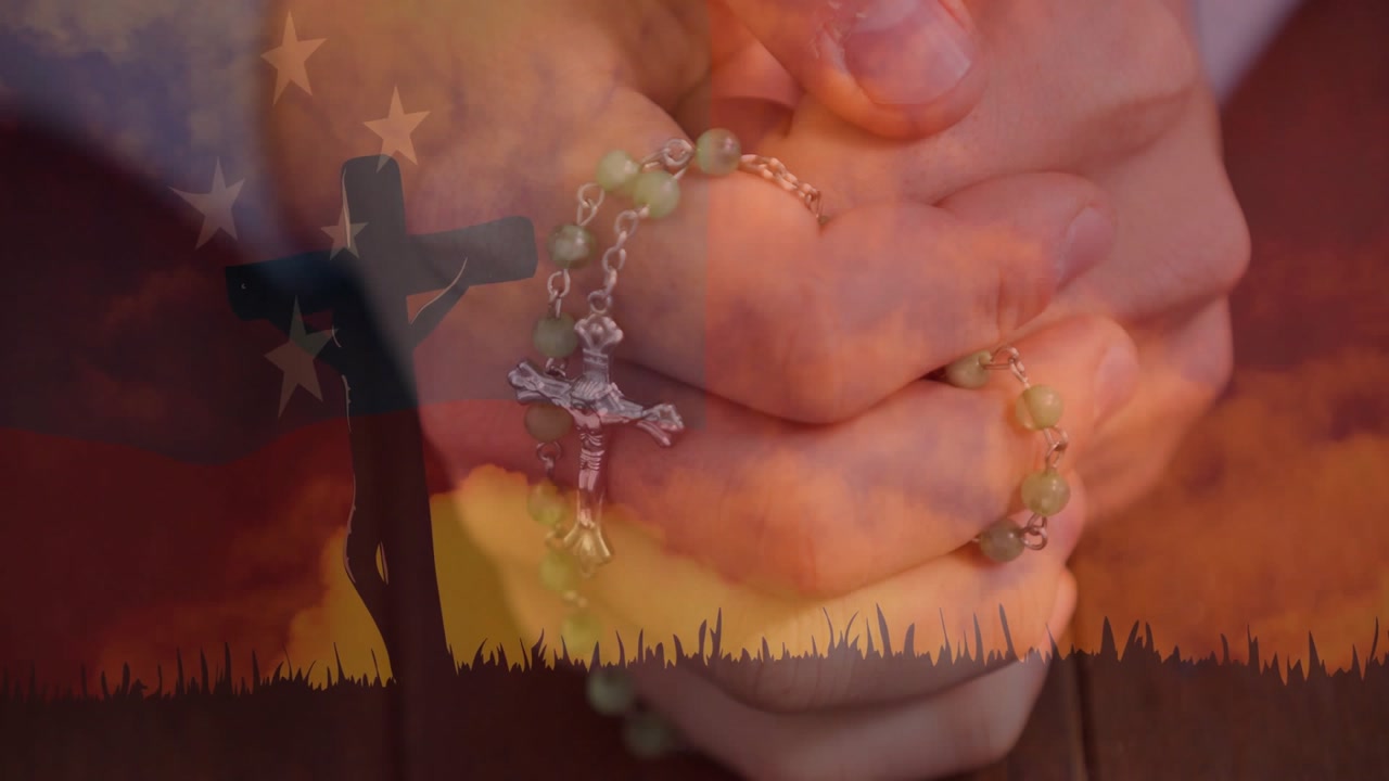 Vertical video: Light shifting causing hands praying with green rosary on wood table with cross