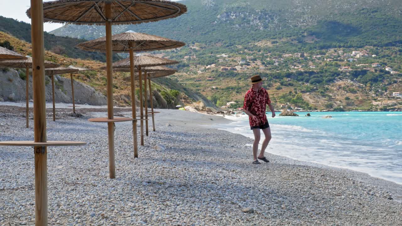 Man Wearing Hat And Summer Beach Floral Outfit Throwing Pebbles Into The Sea In Agia Kiriaki Beach, Zola, Kefalonia, Greece