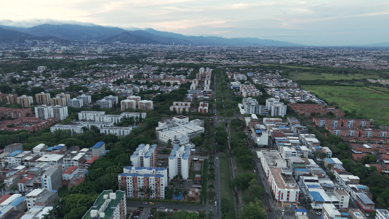 Drone footage over Valle del Lili in Valle del Cauca reveals an expansive urban landscape, showcasing residential and commercial areas under soft evening light, framed by distant mountains