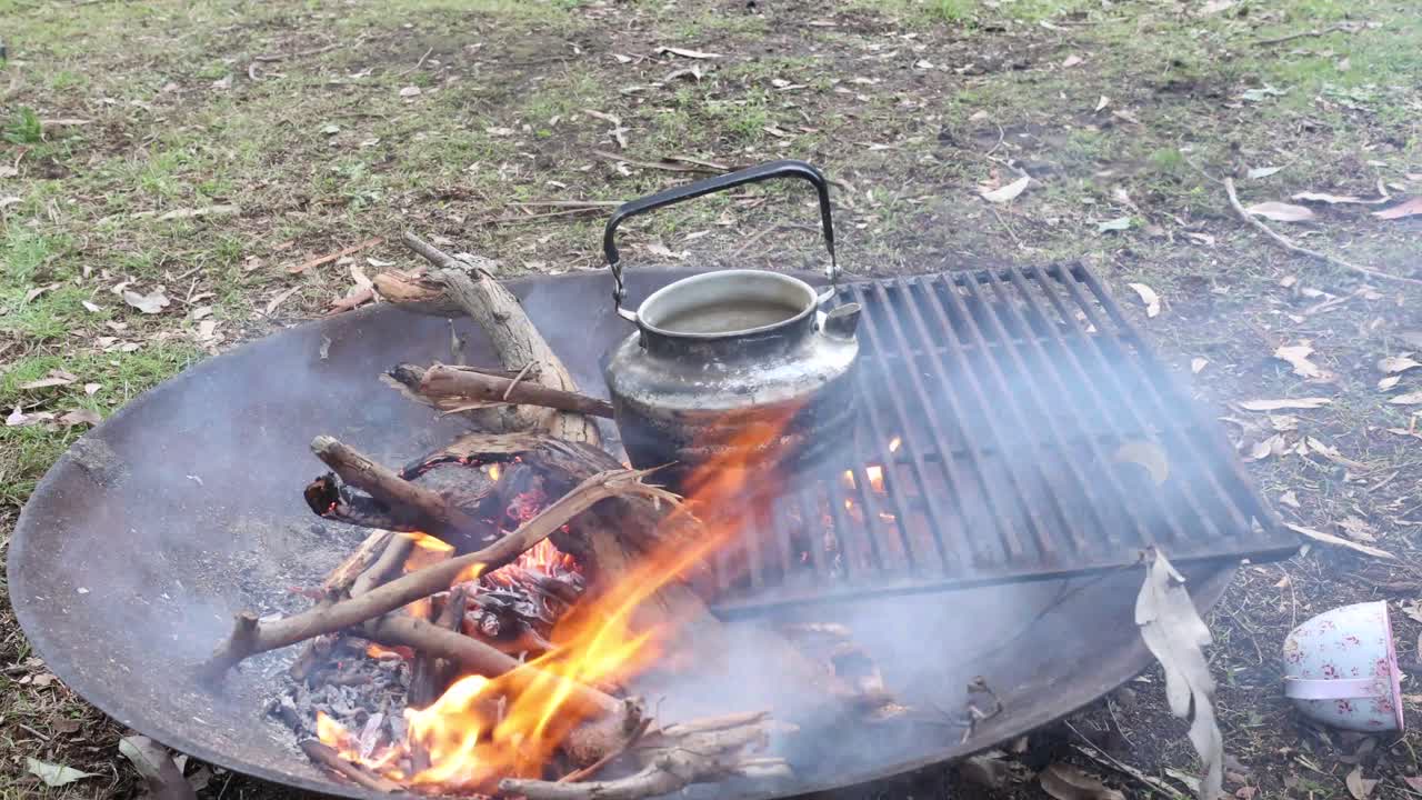 A tradtional australian billy tea pot boiling on a camp fire out in the bush.