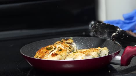 chef flips chicken breasts on a pan using tongs as they cook and steam coating the delicious dinner time meal with a mouth-watering crispy texture and seasoned with thyme, food closeup
