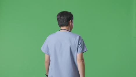 back view of asian male doctor with stethoscope waving hand and smiling while walking on green screen background in the hospital