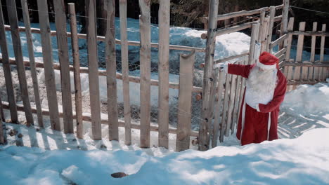 santa is walking on a snowy path along a wooden fence