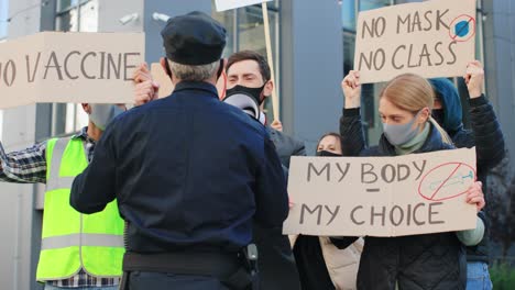 полицейский останавливает группу людей во время демонстрации против ковида 19 на улице