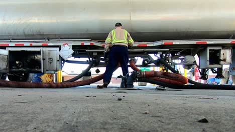 material de archivo de ángulo bajo de alta definición de un conductor descargando combustible utilizando mangueras de un camión cisterna de combustible de remolque de tractor