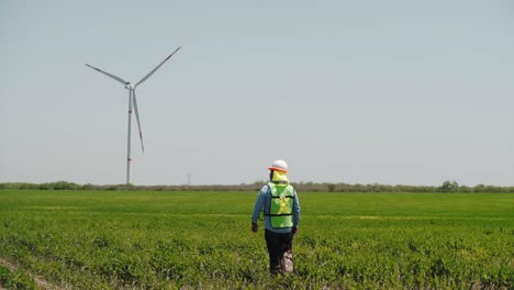 Trabajador-Caminando-En-Un-Campo-Frente-A-Turbinas-Eólicas-De-Un-Parque-Eólico,-México