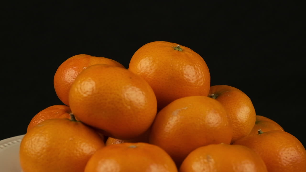 una placa de naranjas clementinas gira aislada sobre un fondo negro