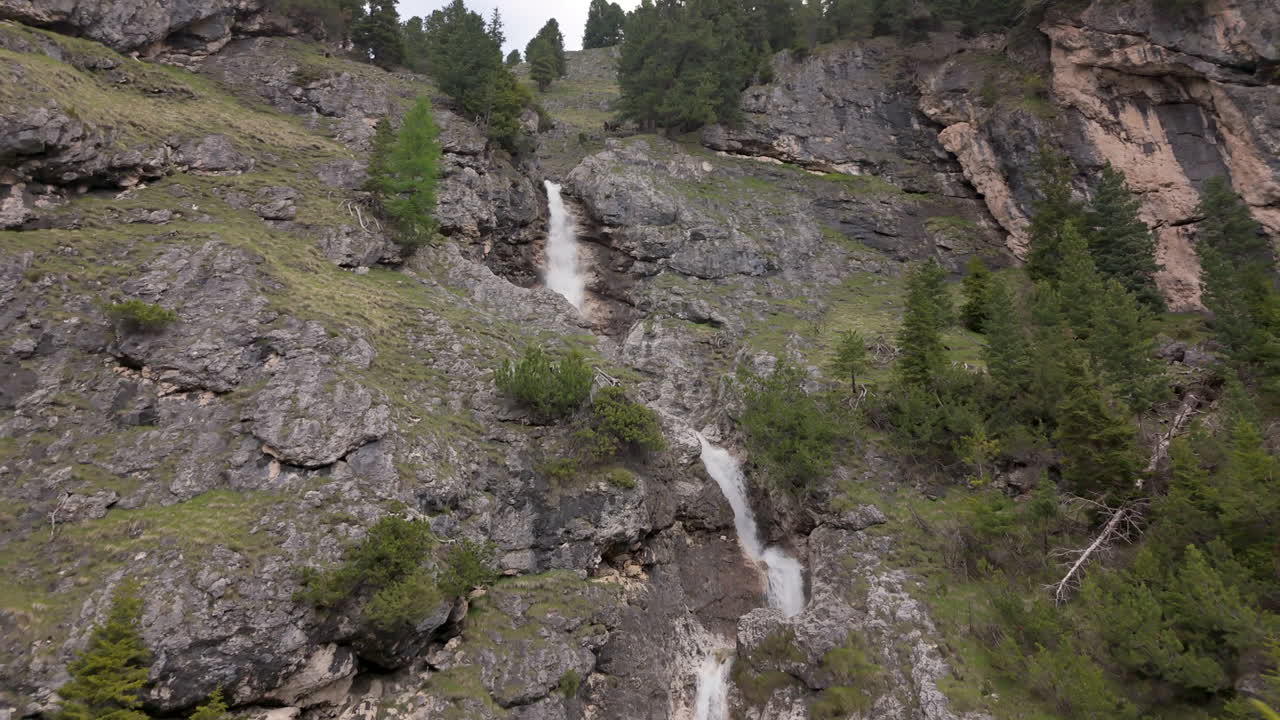 Et vakkert fossefall fosser ned et steinete fjell, omgitt av frodig grønt i Dolomittene