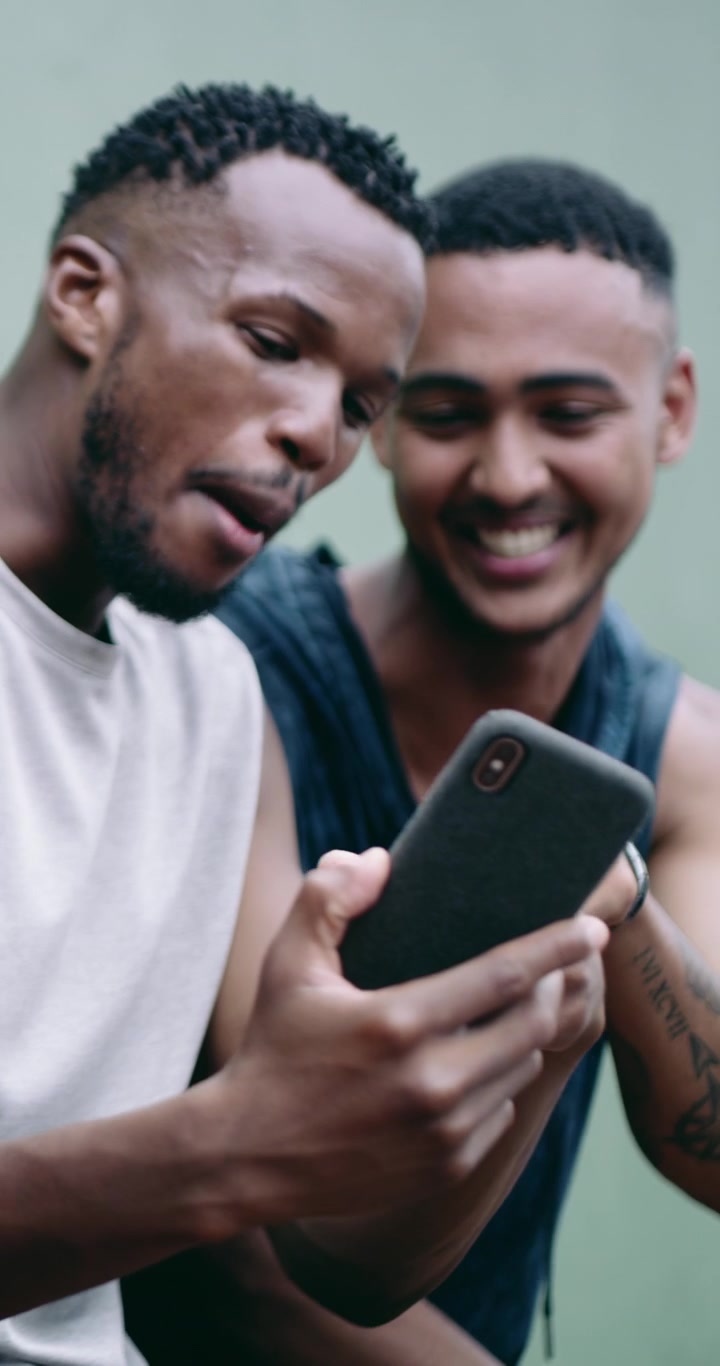 Two Young Men Laughing and Looking at a Smartphone Together