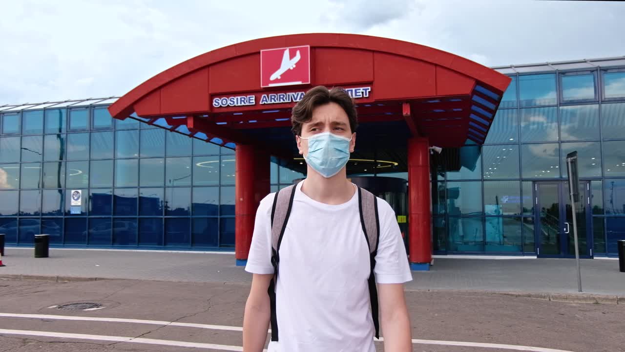 CHISINAU, MOLDOVA - JUNE 19, 2020: Man with a white t-shirt, backpack and surgical mask walking away from airport. Traveling during Corona Virus pandemic outbreak. Chisinau, Moldova